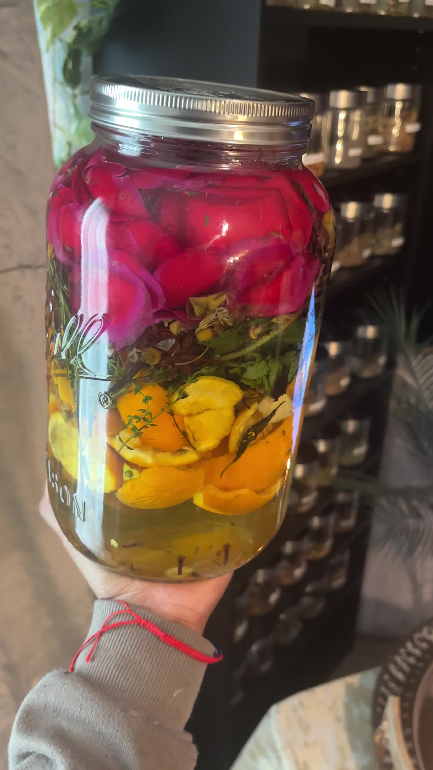 My homemade Florida Water in a glass jar, with layers of citrus peel, herbs, and red rose petals.